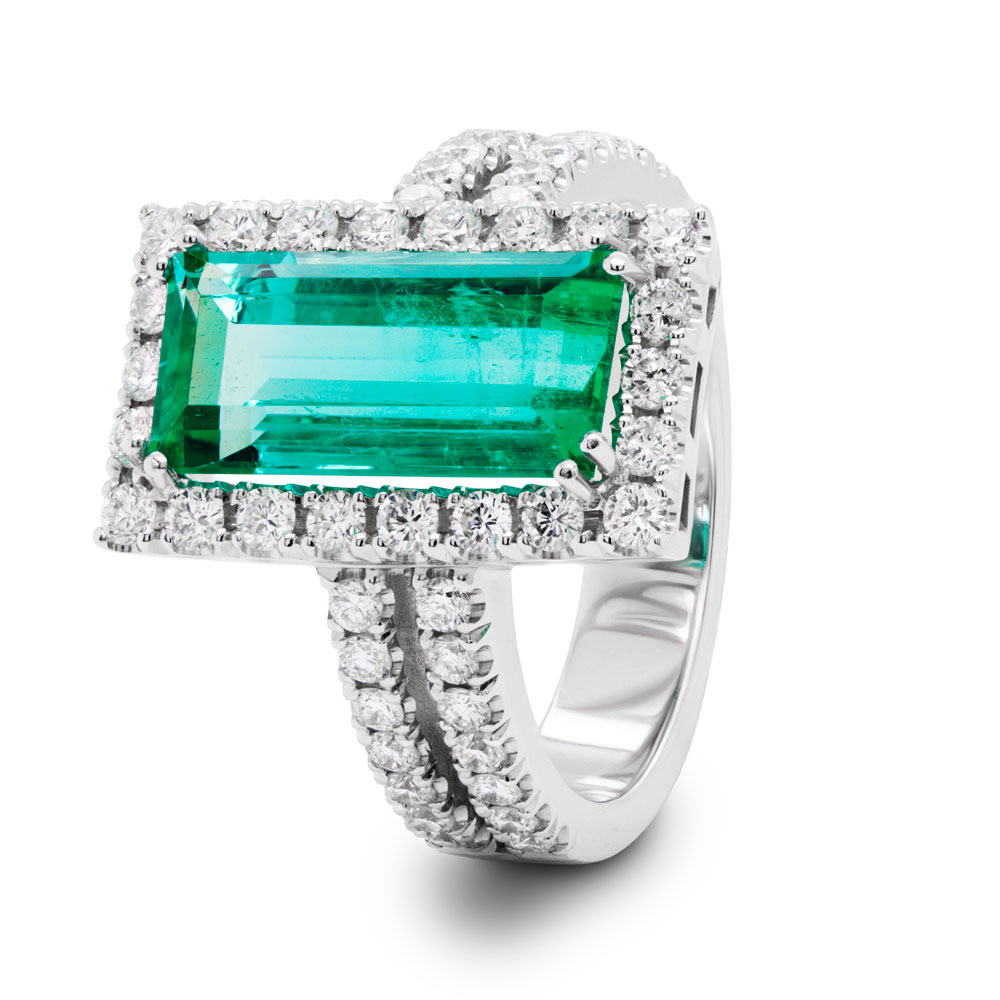 Photo of a emerald cut emerald halo style ring in white gold on a white background.